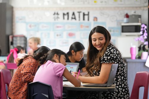A smiling elementary school teacher sits with her engaged students