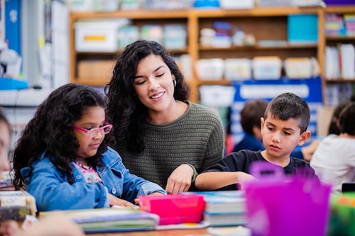 A teacher smiles works with her a diverse group of students.