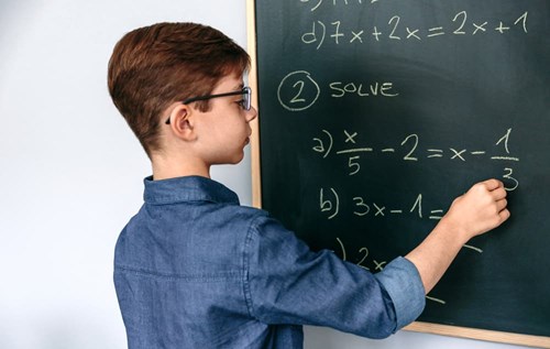 A young student works math problems on a chalkboard
